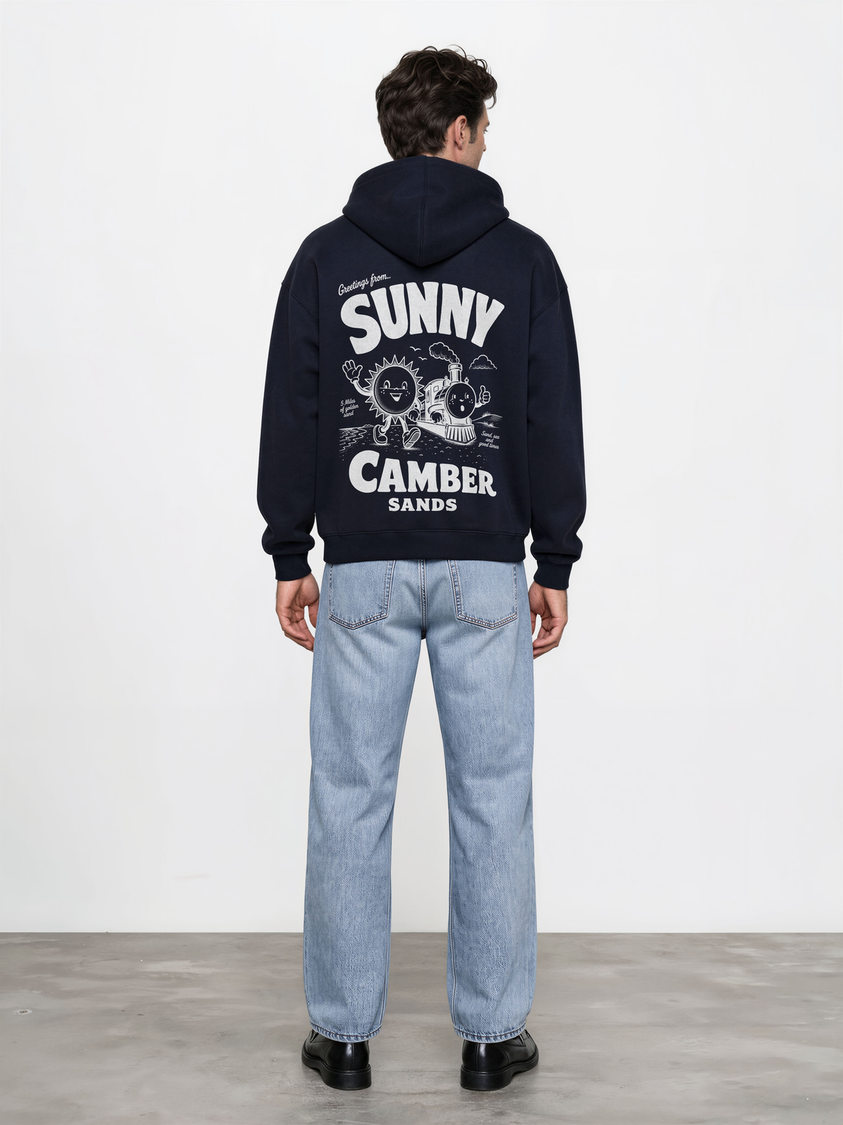 Sunny Camber Sands navy hoodie, back male model view, showing the larger white seaside sun and steam train back design