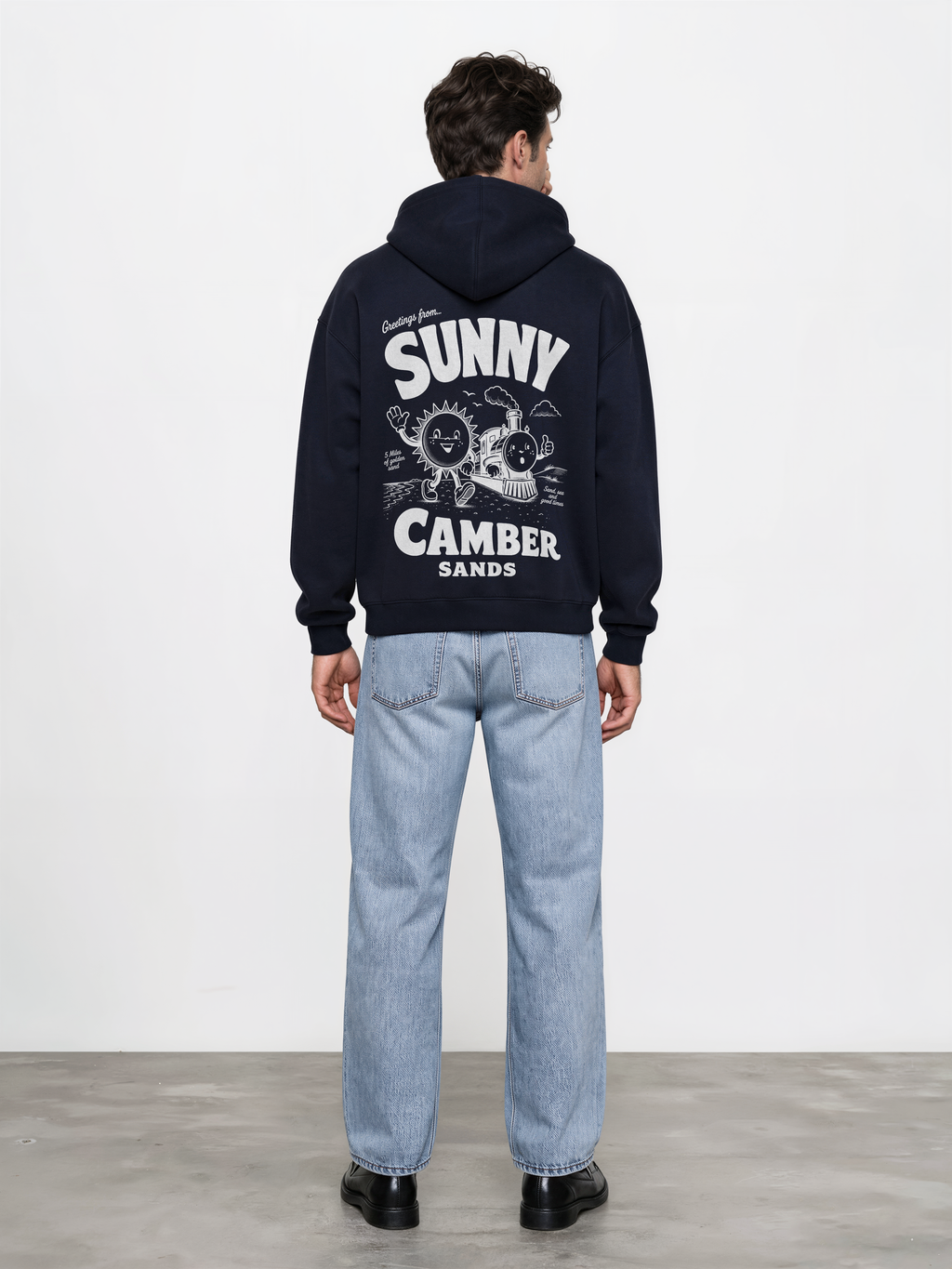Sunny Camber Sands navy hoodie, back male model view, showing the larger white seaside sun and steam train back design