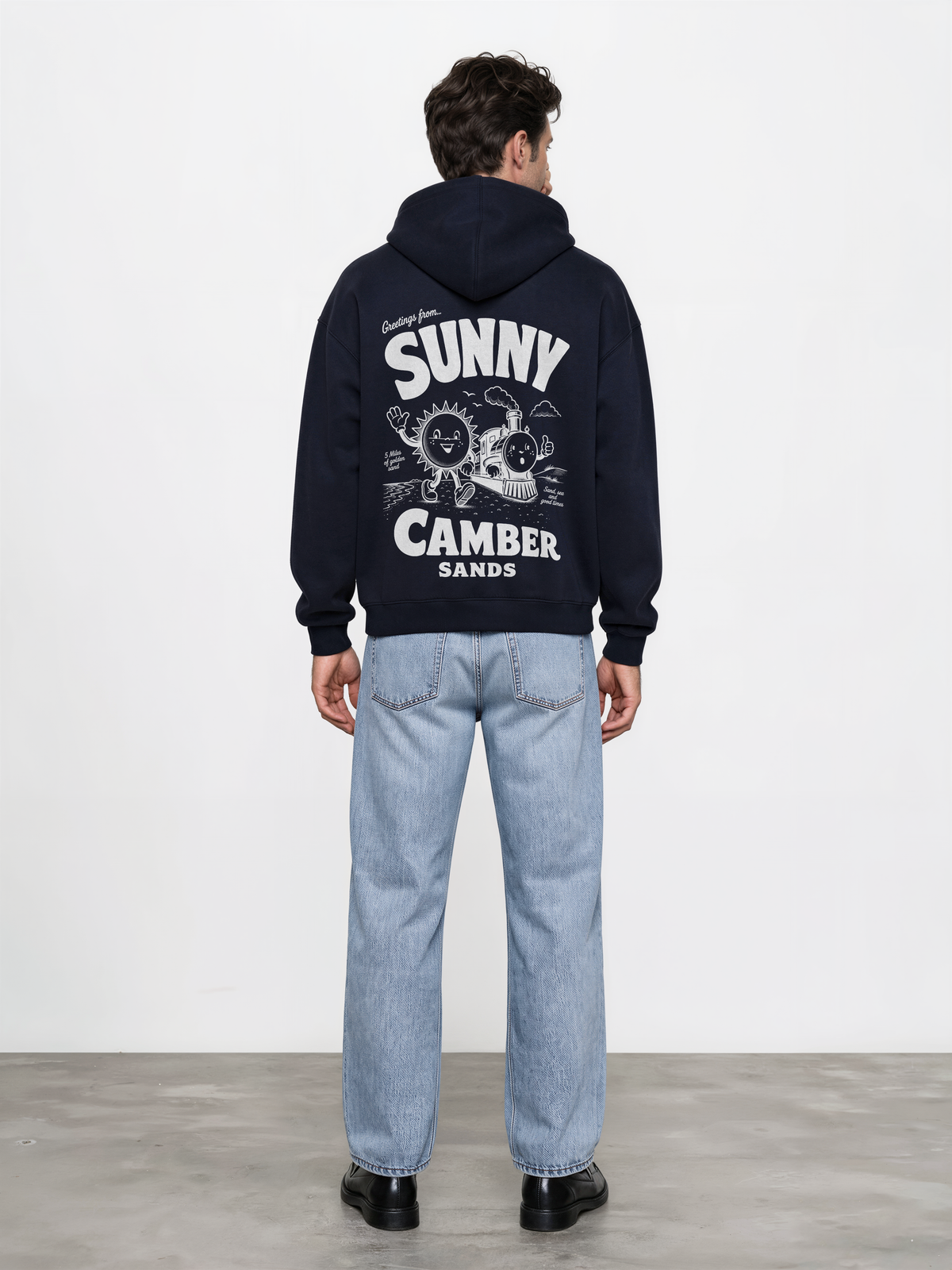 Sunny Camber Sands navy hoodie, back male model view, showing the larger white seaside sun and steam train back design