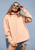 Model wears peach hoodie with plain front in sunshine, print to the back of hoodie