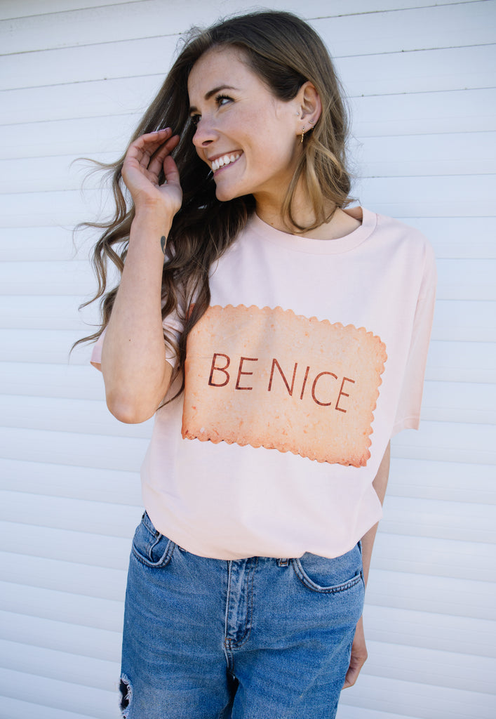 model is wearing peach coloured organic t shirt with photo print biscuit and be nice slogan