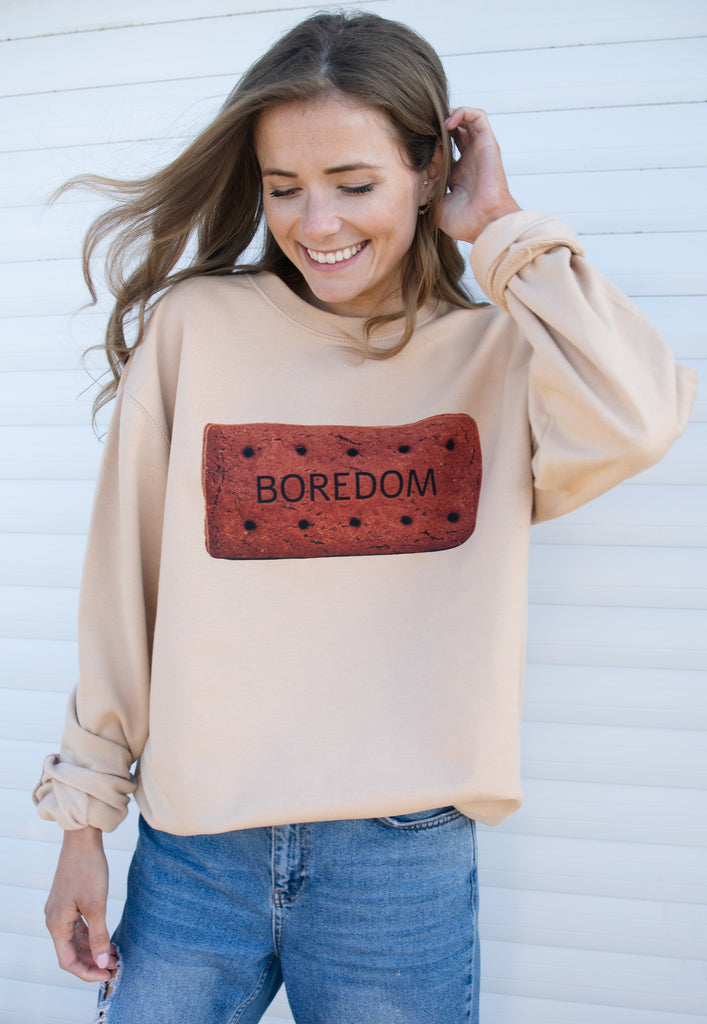 Model wears natural colour sweater with "Boredom" slogan and biscuit graphic