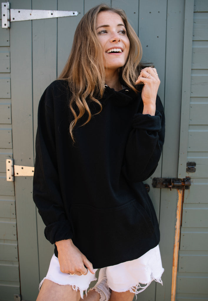 model is wearing black hoodie showing plain front view, large graphic print can be seen on back of garment