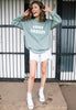 model is wearing pastel spring sweatshirt printed with bring snacks slogan in white 