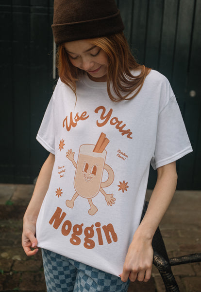 female model wears vintage style christmas t shirt printed with "use your noggin" slogan and egg nog character 