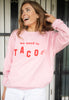 Model wears pink sweatshirt with we need to taco slogan in red print