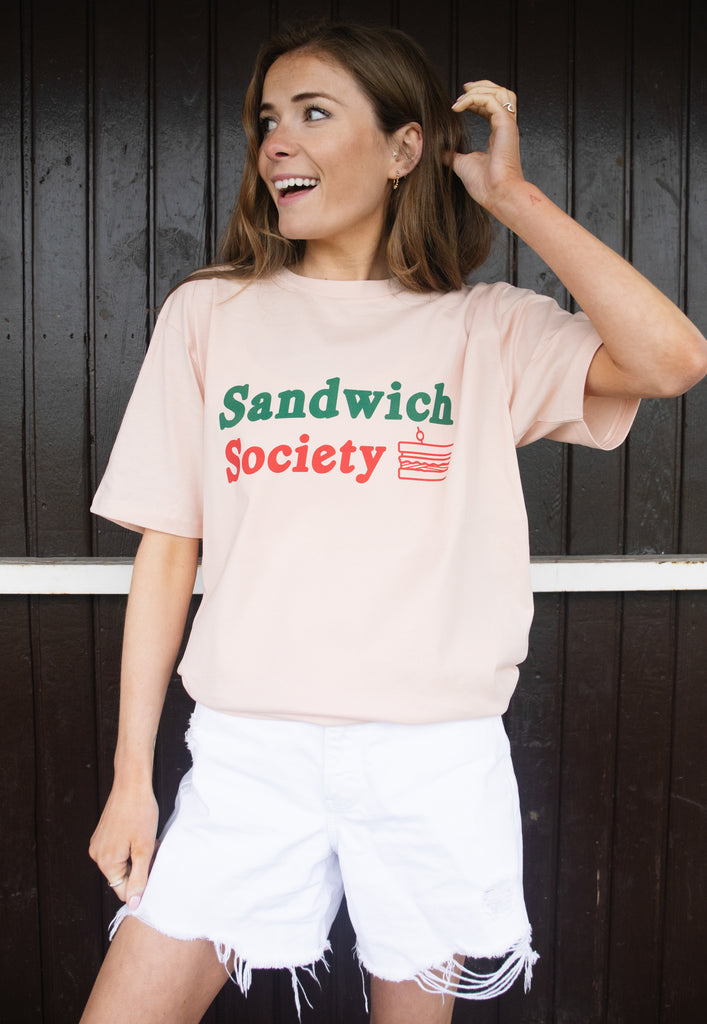 Model wears organic peach coloured t-shirt with sandwich society slogan printed on front