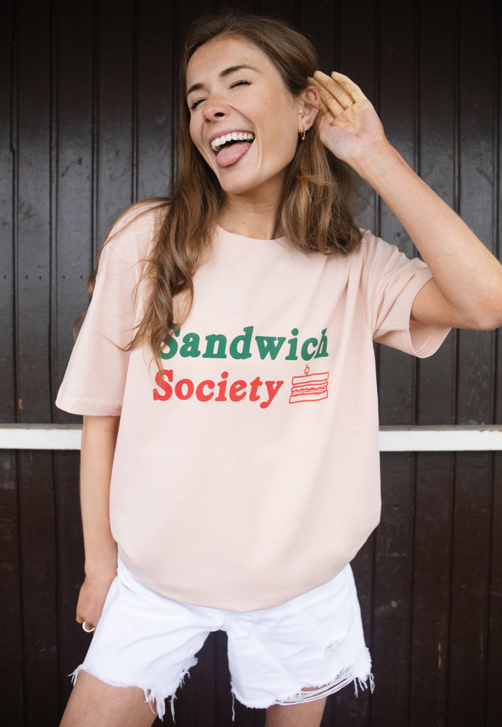 Model wears relaxed, fun peach t-shirt printed with sandwich society slogan 