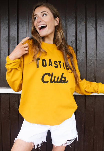 Model wears mustard sweatshirt with Toastie Club slogan 