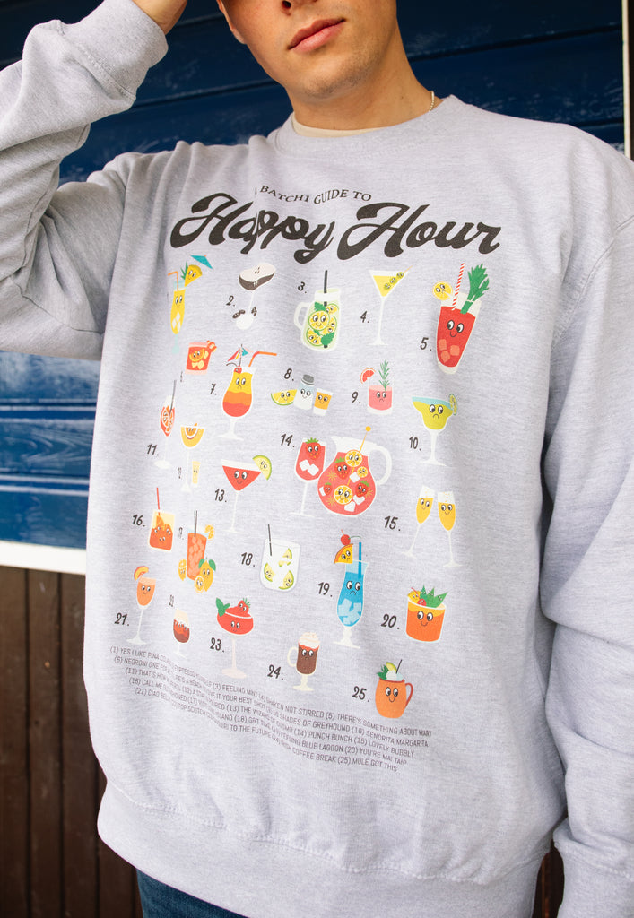 Model wears grey sweatshirt with Happy Hour slogan and cocktail guide character graphic