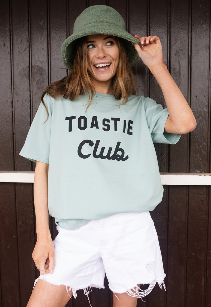 Model wears dusty green tshirt with Toastie Club slogan 