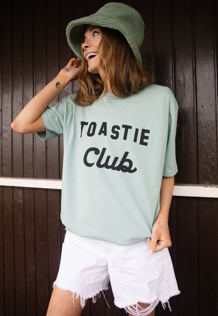 Model wears dusty green tshirt with Toastie Club slogan 