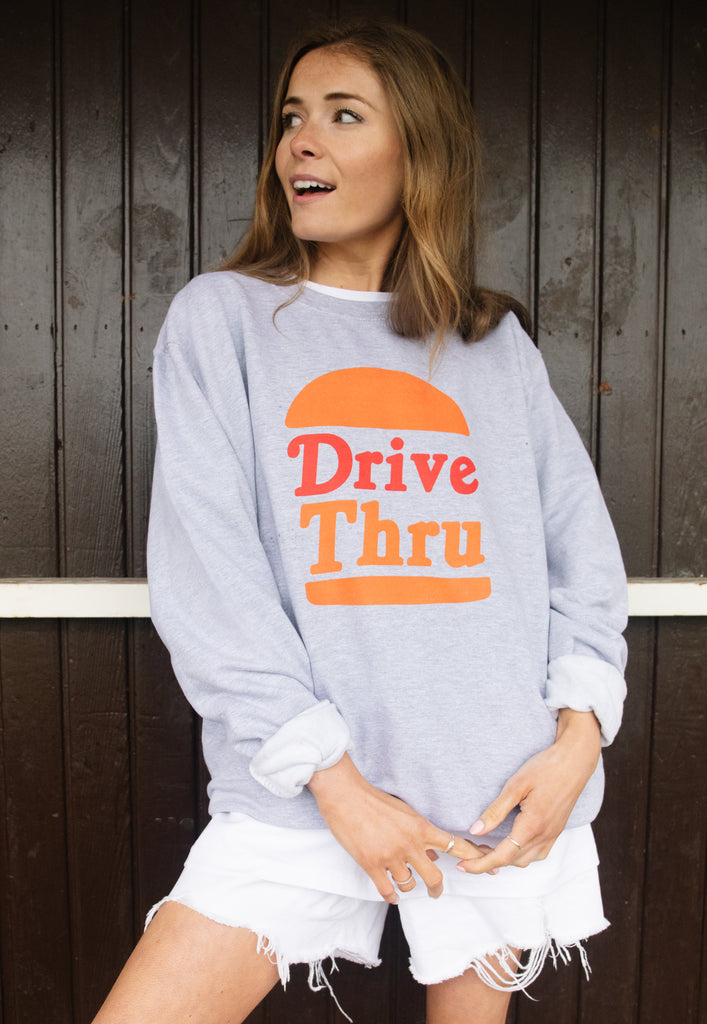 Model wears grey sweatshirt with Drive Through slogan and burger graphic 