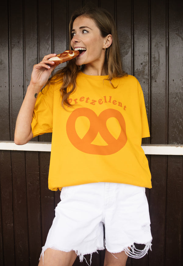 Model wears mustard shirt with Pretzellent slogan with pretzel graphic 