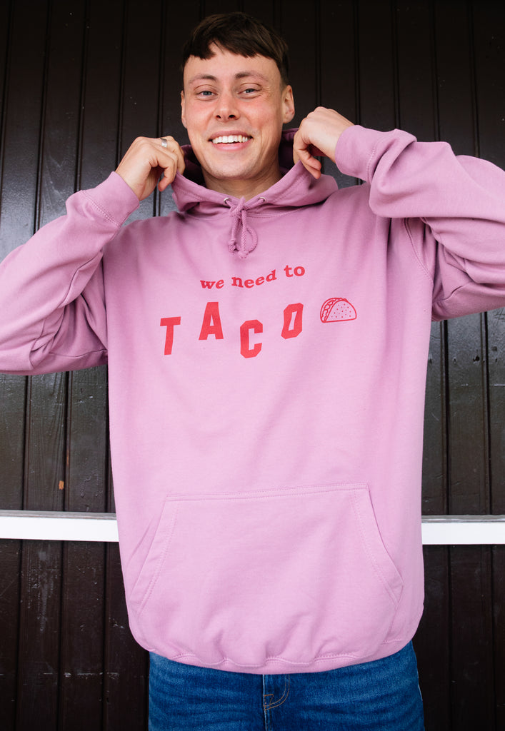 Model wears dusty purple hoodie with We Need To Taco slogan and taco graphic 