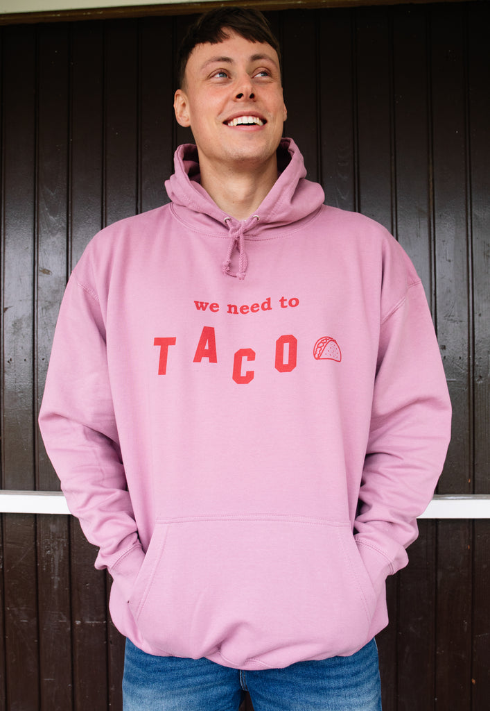 Model wears dusty purple hoodie with We Need To Taco slogan and taco graphic 