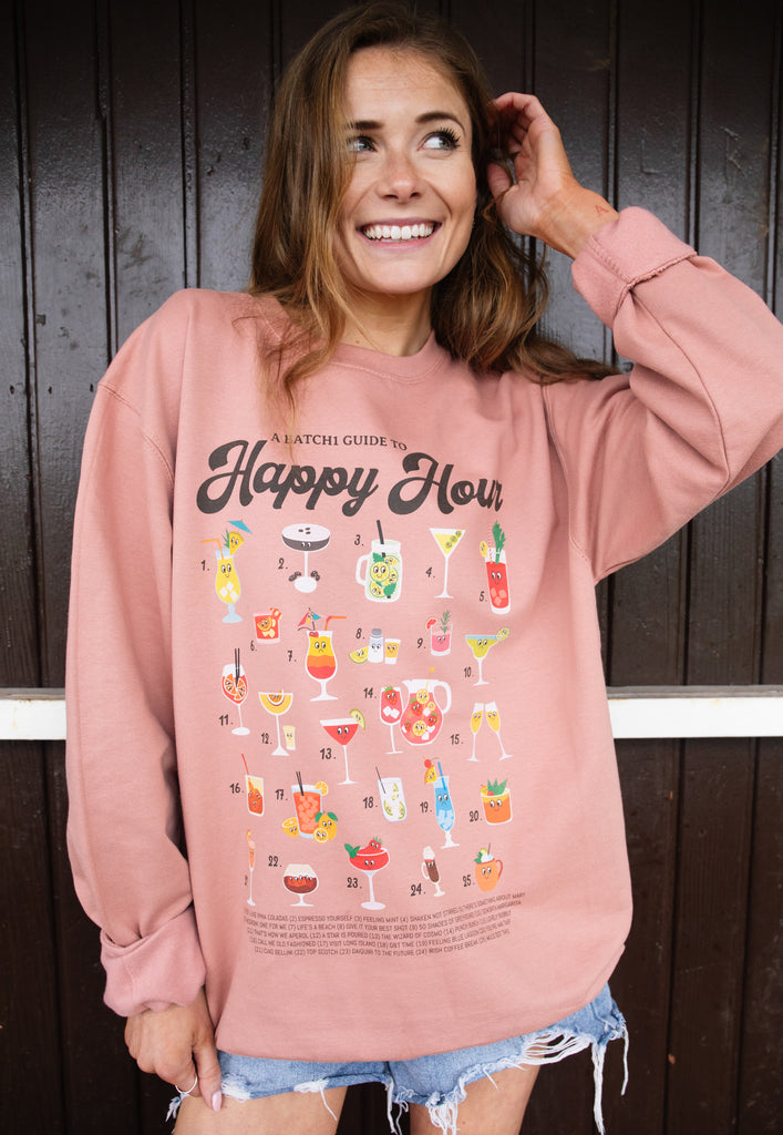 Model wears dusty pink sweatshirt with Happy Hour slogan andcocktail guide print