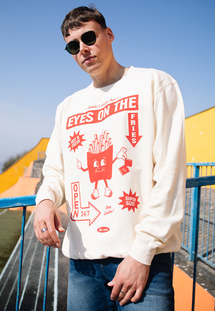 Model wears vanilla sweatshirt with Eyes on the Fries slogan and french fries character graphic 
