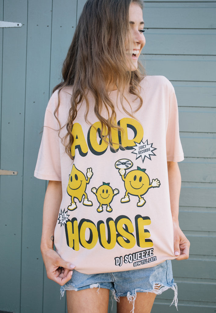 Model wears organic peach coloured t-shirt with printed "acid house" slogan and fruit characters on front