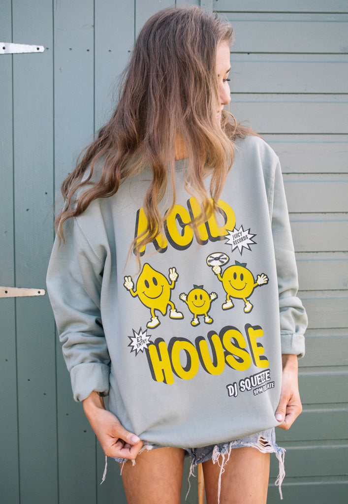 Model shown wearing dusty green festival sweater with printed "acid house" slogan and fruit graphics