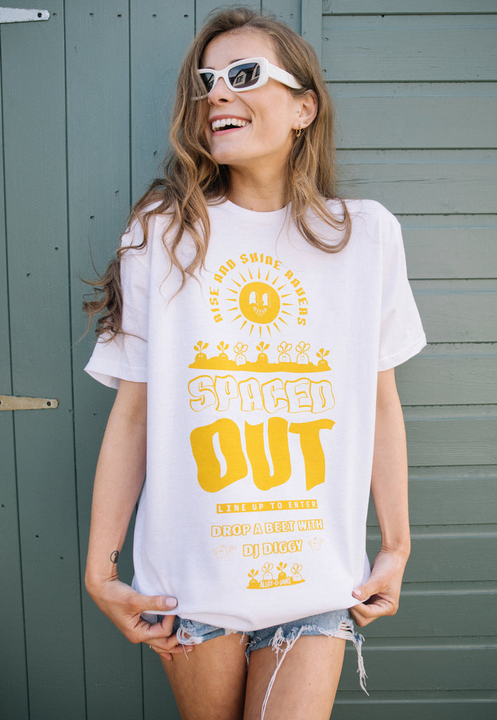 Model wearing white summer tee with printed festival style graphics showing sunshine, vegetables and spaced out slogan