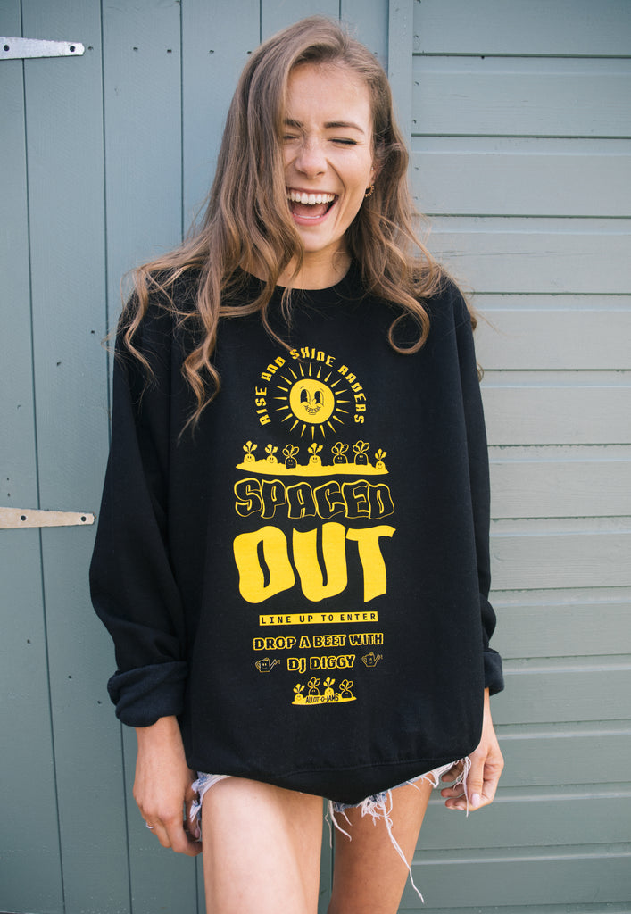 Model wears black festival sweatshirt with "spaced out" slogan and vegetable graphics in bright yellow print 