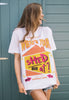 Model wears white unisex fit t-shirt with printed 'where's your shed at' slogan and 90s festival graphics