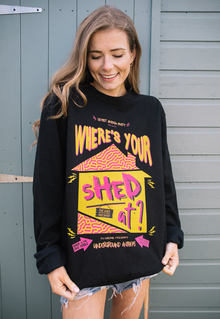 Model is wearing black festival sweater printed with bright pink and yellow graphics, "Where's your shed at" slogan and shed picture