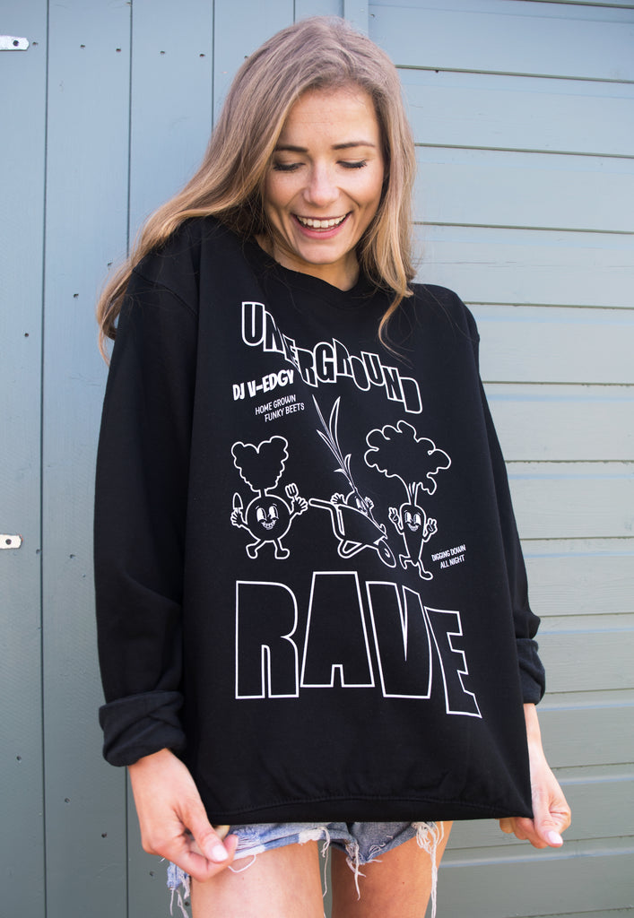 Model wears casual printed relaxed fit sweater with festival style print and 'underground rave' slogan with dancing veggies!