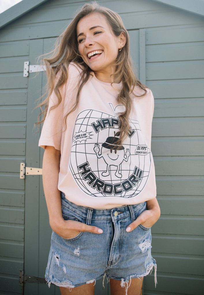 Model wears organic cotton printed tee with 90s graphics showing apple character and "Happy Hardcore" slogan