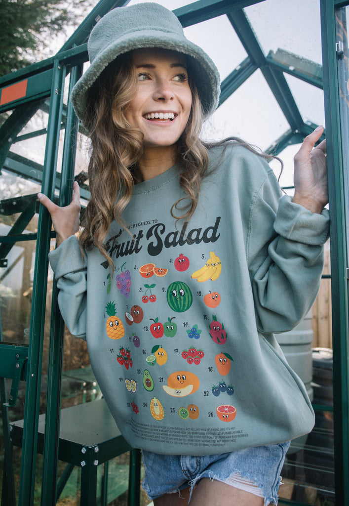 Model wears pastel green sweater with "Fruit salad" slogan and fruit character graphics