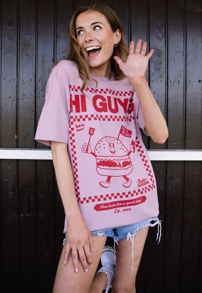 Model wears dusty purple tshirt with Hi Guys slogan and burger character graphic