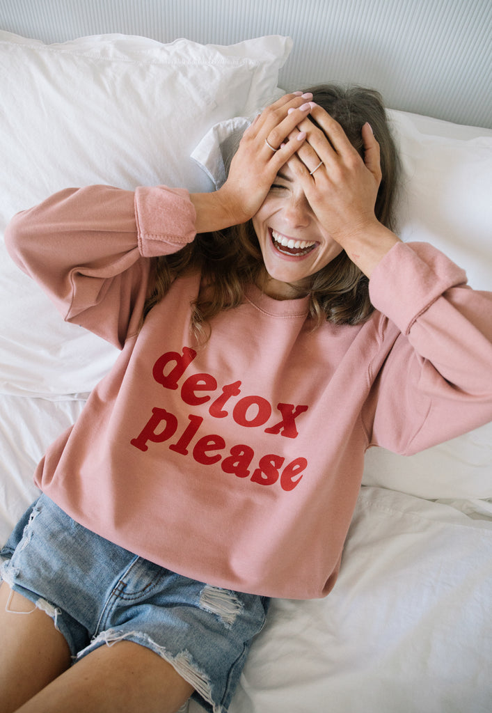 Model wears dusty pink sweatshirt with printed Detox Please slogan in red text to front