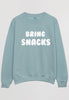 Flatlay of pastel green sweatshirt with bring snacks slogan in white print