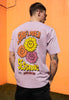 male model wears casual purple t shirt with large back print showing colourful sunflower festival poster graphics 